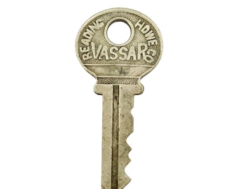 Könnte beinhalten: Ein Vintage-Metallschlüssel mit dem Text "READING HOWE VASSARS" auf dem Kopf eingraviert. Der Schlüssel hat ein kreisförmiges Loch oben und eine gezackte Kante entlang der Klinge. Der Schlüssel ist silberfarben.