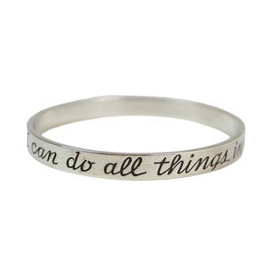 Può includere: Un braccialetto a cerchio color argento con l'iscrizione "I can do all things in" in un carattere scritto a mano. Il braccialetto è circolare e si trova su uno sfondo bianco.