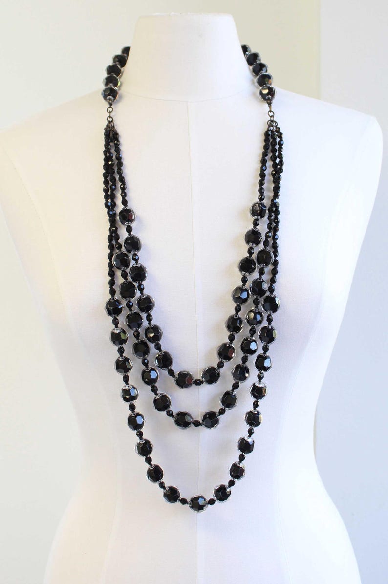 May include: A multi-strand necklace with large, faceted black beads. The necklace is made of several strands of beads, creating a layered look.