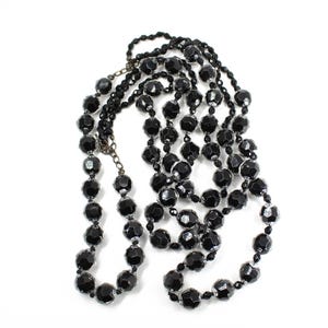 May include: A long black beaded necklace made of faceted glass beads. The necklace is layered and has a simple design.