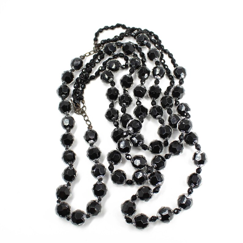 May include: A long black beaded necklace made of faceted glass beads. The necklace is layered and has a simple design.