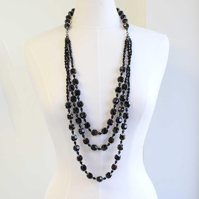 May include: A multi-strand necklace made of black beads. The necklace is layered and features a long, flowing design.