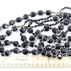 May include: A long strand of black glass beads with a faceted finish. The beads are approximately 1/2 inch in diameter and are strung on a silver-toned chain.