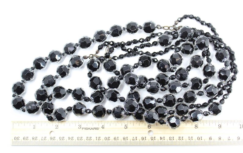 May include: A long strand of black glass beads with a faceted finish. The beads are approximately 1/2 inch in diameter and are strung on a silver-toned chain.