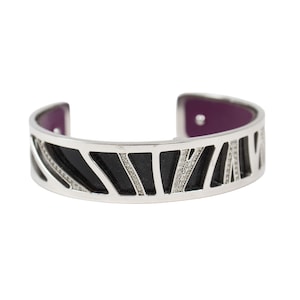 May include: Silver-tone cuff bracelet with a geometric design. The bracelet features black and diamond-like accents, with a purple interior. A stylish piece of jewelry.
