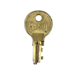 Puede incluir: Una llave de latón antigua con la palabra "PRESTO" grabada en la cabeza. La llave tiene una cabeza circular con un agujero y una superficie texturizada. El vástago de la llave tiene una serie de muescas y crestas.