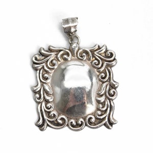 May include: Silver pendant with an ornate, scrolled frame and a smooth, oval-shaped center.