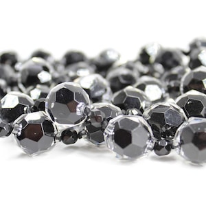 May include: A strand of black and clear faceted glass beads. The beads are round and have a shiny finish.