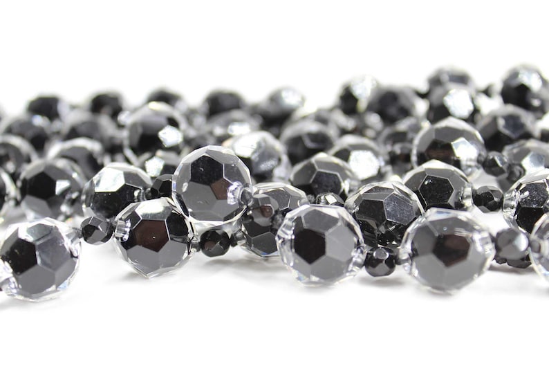 May include: A strand of black and clear faceted glass beads. The beads are round and have a shiny finish.