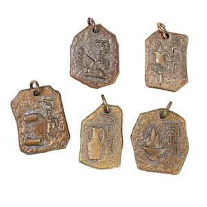May include: A collection of five bronze-colored pendants with various embossed designs. Each pendant has a unique shape and features symbols like a scroll, a vase, a flame, and a bird with a wing. They have a textured surface and a small loop for hanging.