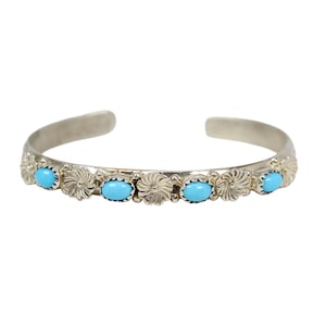 Może przedstawiać: Srebrna bransoletka z turkusami. Bransoletka ma kwiatowy wzór z owalnymi turkusami umieszczonymi pośrodku każdego kwiatu. Bransoletka jest otwarta na końcach.
