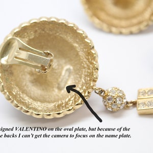 May include: Gold tone clip-on earrings with a black stone and crystal accents. The back of the earring is marked "VALENTINO".