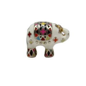 Può includere: Piccola statuetta di elefante bianco con motivi geometrici colorati sulla schiena e sulle zampe. L'elefante ha una zanna dorata ed è decorato con accenti rossi, rosa e neri. La statuetta è un oggetto decorativo.