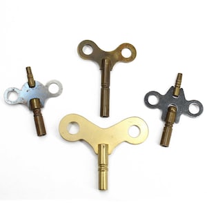 May include: Three vintage clock winding keys. Two are brass with a T-shaped handle and one is silver with a round handle.