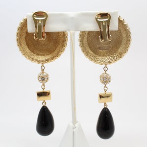 May include: Gold tone clip-on earrings with a black teardrop pendant, a small round crystal cluster, and a rectangular gold piece.