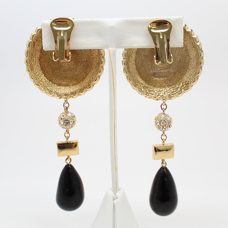 May include: Gold tone clip-on earrings with a black teardrop pendant, a small round crystal cluster, and a rectangular gold piece.