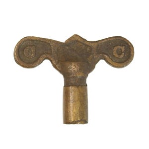 May include: A vintage brass clock key with a decorative, symmetrical design. The key features a T-shaped handle with scrolled ends and a cylindrical stem. The brass has a tarnished, aged appearance, suggesting its antique nature.