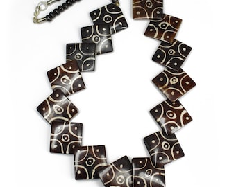 May include: A brown and white patterned necklace with square beads. The beads have a geometric design with white circles on a brown background.