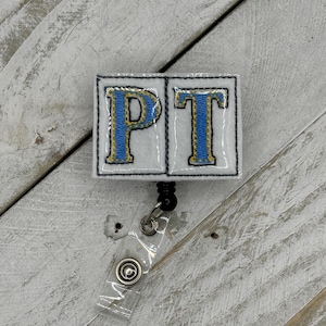 Puede incluir: Porta credencial blanco con un "PT" bordado en azul y amarillo. El porta credencial está unido a un carrete retráctil de credencial de plástico transparente.