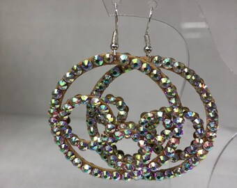 May include: A pair of large, round, gold-toned earrings with iridescent rhinestones. The earrings are made of two overlapping circles, each adorned with rhinestones.