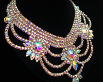 May include: A multi-layered iridescent crystal rhinestone necklace with a V-shaped neckline. The necklace features a central design with three large crystals and smaller crystals arranged in a floral pattern.