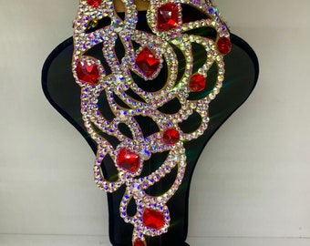 Peut inclure: Un grand collier orné de cristaux rouges et transparents avec un design délicat et complexe. Le collier est présenté sur un buste de mannequin en velours noir.