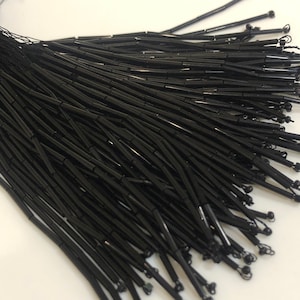 May include: A bunch of black glass beads, each bead is a long cylinder shape.