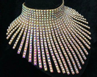 May include: A tan leather choker necklace with iridescent rhinestones. The necklace is designed in a fan shape with the rhinestones forming rows that radiate out from the center.