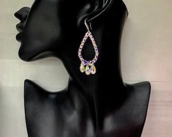 May include: A pair of silver teardrop earrings with a clear crystal teardrop design. The earrings are adorned with smaller clear crystals and purple accents.