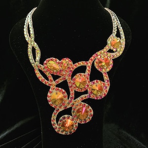 Peut inclure: Un collier délicat à plusieurs rangs avec un motif floral. Le collier est composé de petits cristaux irisés dans les tons orange, rouge et jaune.