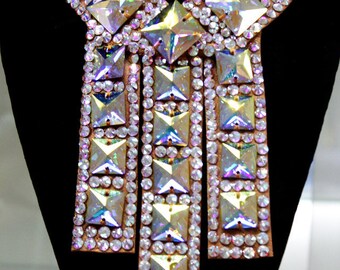 May include: A large, ornate, iridescent crystal necklace with a star-shaped center piece. The necklace is made of many small, square crystals and is designed to be worn as a statement piece.