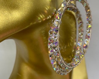 May include: A pair of large, silver hoop earrings with a double row of iridescent rhinestones.