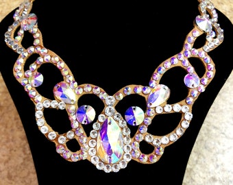 May include: A brown fabric base with a crystal rhinestone design. The rhinestones are clear with iridescent rainbow colors.