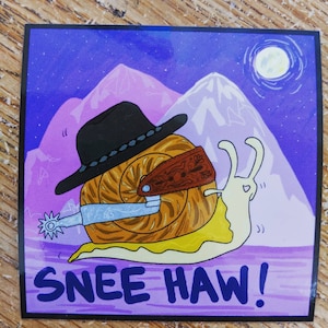Może przedstawiać: Kreskówkowy ślimak w kowbojskim kapeluszu i trzymający ostrogę. Ślimak znajduje się na fioletowym tle z górami i księżycem w tle. Tekst "Snee Haw!" jest napisany pod ślimakiem.