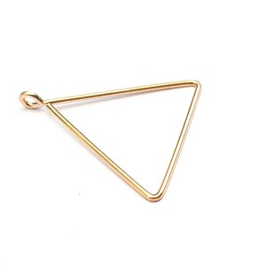 May include: A gold-colored, open-frame triangle pendant with a small loop at the top for attaching to a chain or cord. The pendant is made of thin wire and has a geometric design. The pendant is suitable for jewelry making.