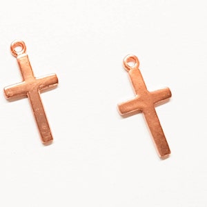 Puede incluir: Dos pequeños dijes de cruz de color oro rosa con un bucle en la parte superior para sujetar a las joyas.