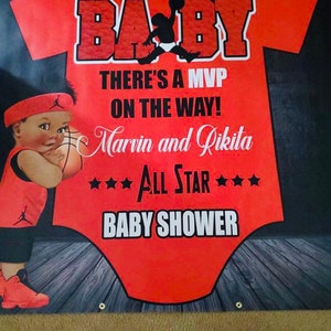 May include: A red and black baby onesie with a basketball theme. The onesie has the word "BABY" in large white letters at the top. The text "THERE'S A MVP ON THE WAY! Marvin and Rikita *ALL STAR* BABY SHOWER" is printed in white on the onesie. A cartoon basketball player is printed on the onesie.