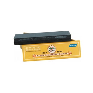 May include: A black combination bench stone with the text "JB-8" and "CRYSTOLON OILSTONE NORTON" on top of a yellow box. The box reads "COMBINATION BENCH STONE" and "175TH ANNIVERSARY EDITION".