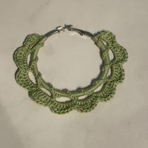 May include: A pair of green crocheted hoop earrings with a silver metal hoop.