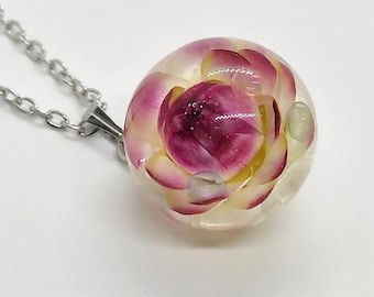 May include: A spherical resin pendant necklace featuring a preserved pink and white flower encased within clear material. The pendant is attached to a silver-toned metal chain with circular links, showcasing the floral details inside the sphere.
