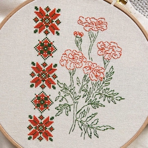 Può includere: Ricamo floreale su tessuto color crema teso in un telaio di legno. Il disegno presenta un motivo verticale di forme geometriche rosse e verdi, accanto a un bouquet di fiori arancioni con steli e foglie verdi.