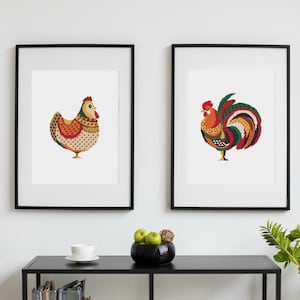 Peut inclure: Deux impressions encadrées représentant des illustrations de style folk art d'une poule et d'un coq. La poule est principalement orange, jaune et marron, tandis que le coq est rouge, vert et jaune. Les deux sont sur fond blanc.