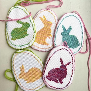 May include: Five handmade Easter egg ornaments with embroidered bunny silhouettes. The bunnies are in shades of green, yellow, pink, purple, and orange.