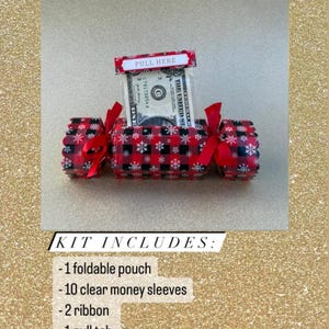 May include: A DIY money pull pouch kit featuring a red and black buffalo plaid pattern with white snowflakes. The kit includes a foldable pouch, ten clear money sleeves, two ribbons, and a pull tab with the text PULL HERE printed on it.