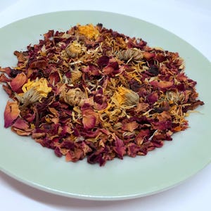 Pode incluir: Um close-up de um prato cheio de pétalas de rosa secas e pétalas de calêndula. As pétalas são uma mistura de vermelho, laranja e amarelo.