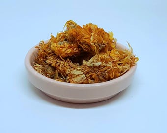 Könnte beinhalten: Eine kleine rosa Schale gefüllt mit getrockneten orangefarbenen Ringelblumenblüten.