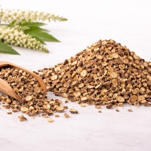 Op de afbeelding: Een witte keramische mok met een zwarte handgreep en de tekst "But First, Coffee" in een vetgedrukte, zwarte letter. De mok staat tegen een vage achtergrond, wat een gezellige setting suggereert.