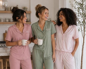 May include: Three sets of short-sleeved button-down pajama shirts and matching pants in dusty rose, sage green, and light pink. The shirts feature notched collars, chest pockets, and embroidered initials AH and KM on the pockets.