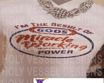 Könnte beinhalten: Weißes T-Shirt mit dem Text "I'M THE RESULT OF GODS Miracle Working POWER" in Rot und Blau. Eine silberne Perlenkette ist über dem Shirt drapiert. Das Design ist mittig auf der Vorderseite platziert.