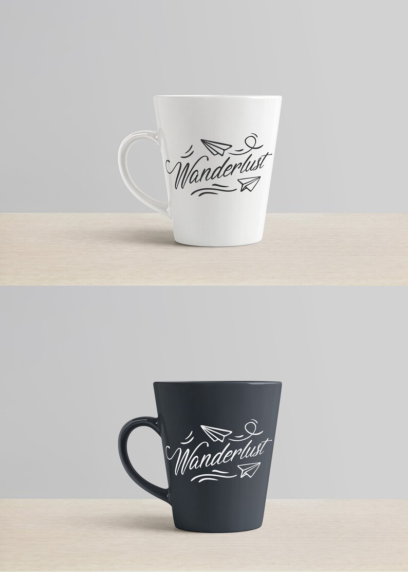 May include: Two ceramic mugs, one white and one dark blue, each with a curved handle. The mugs feature the word "Wanderlust" in cursive, along with paper airplane illustrations. The mugs are on a light wooden surface.